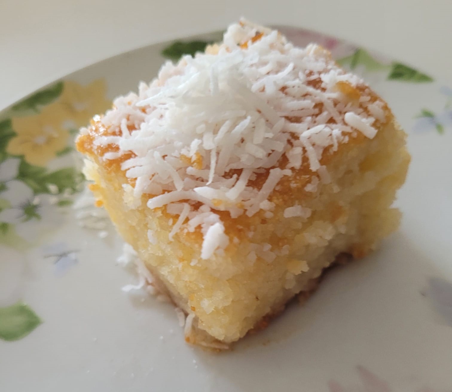 Revani semolina cake slice — golden, syrup-soaked square topped with shredded coconut